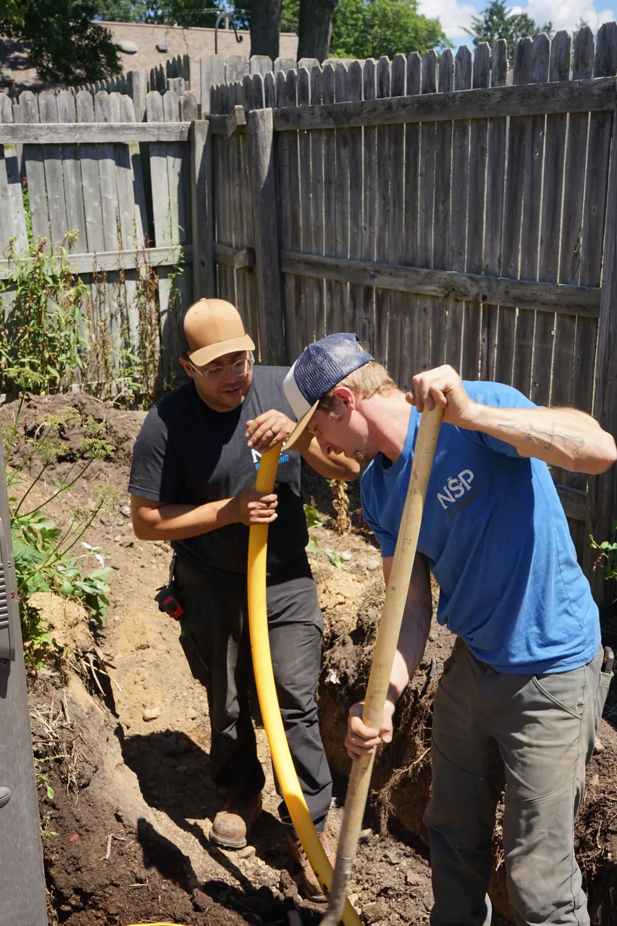 NSP Plumbing plumbers laying new yellow underground gas line in a backyard trench