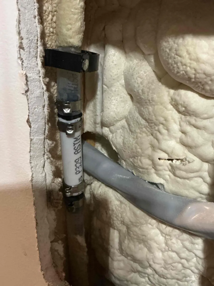 Opened drywall exposing a repaired water pipe inside an outside wall filled with spray foam insulation