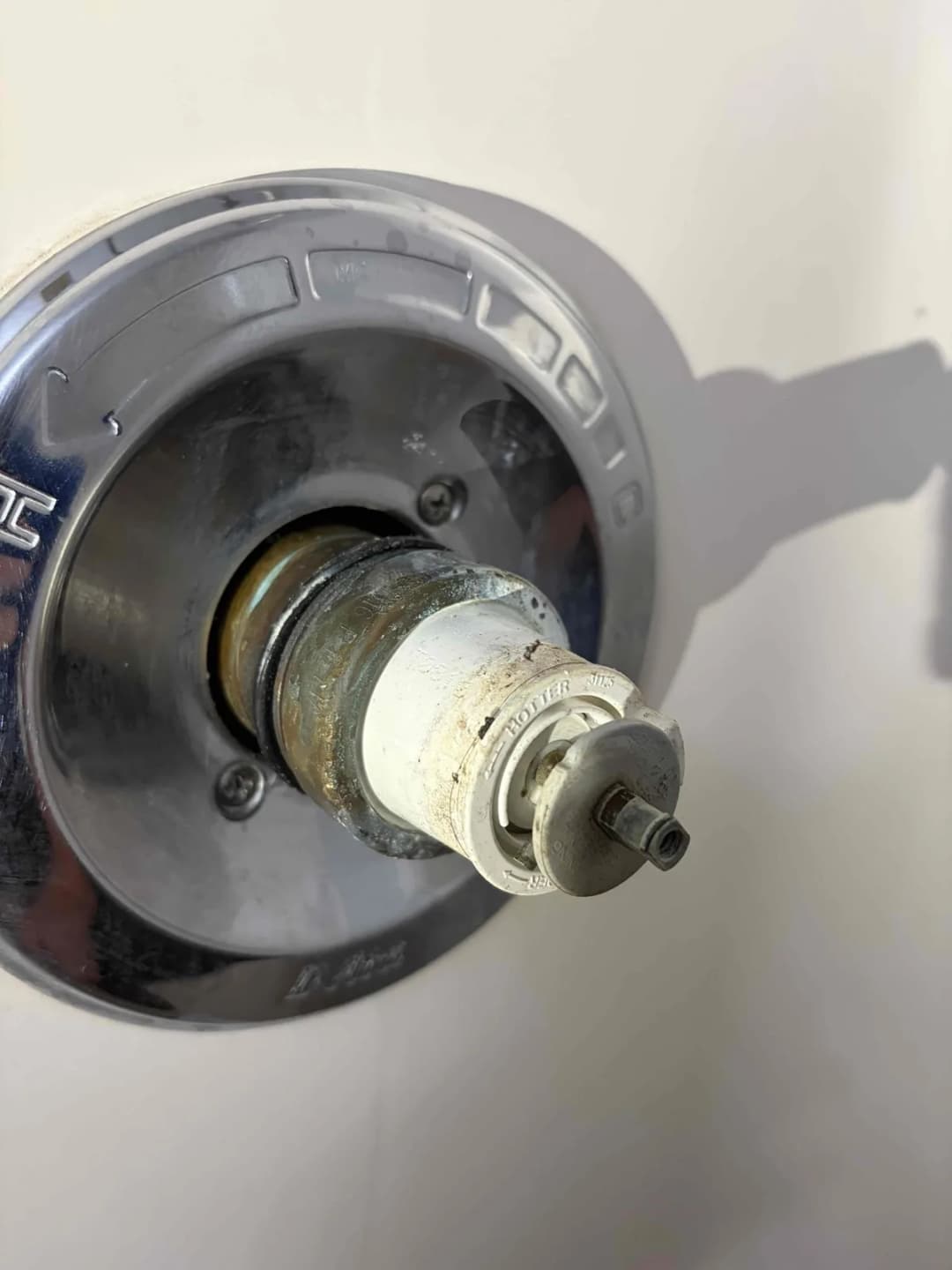Shower cartridge sticking out of the valve with the handle removed and the trim plate still on the wall