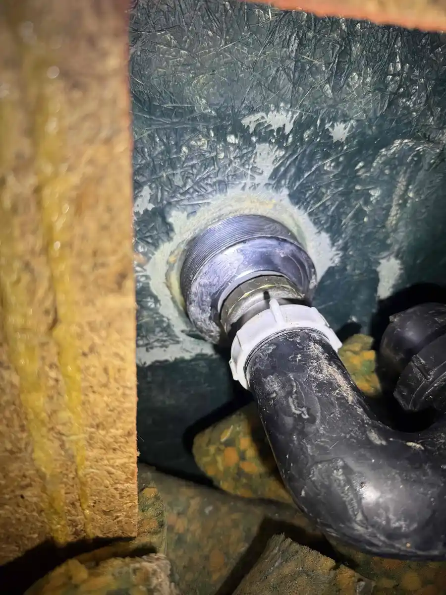 Shower drain connection seen from underneath through a ceiling opening with the drain pipe joined to the bottom of the shower base