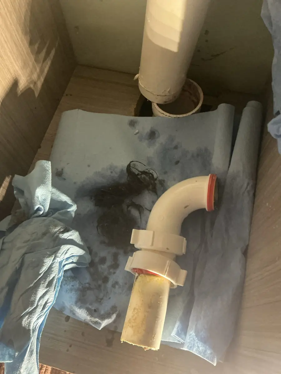 Shower drain trap pipe removed from under a shower with hair and sludge on a drop cloth