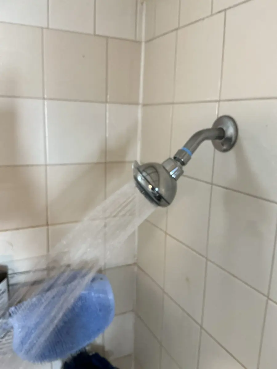 Chrome showerhead spraying a thin, weak stream into a tiled shower during a low pressure test