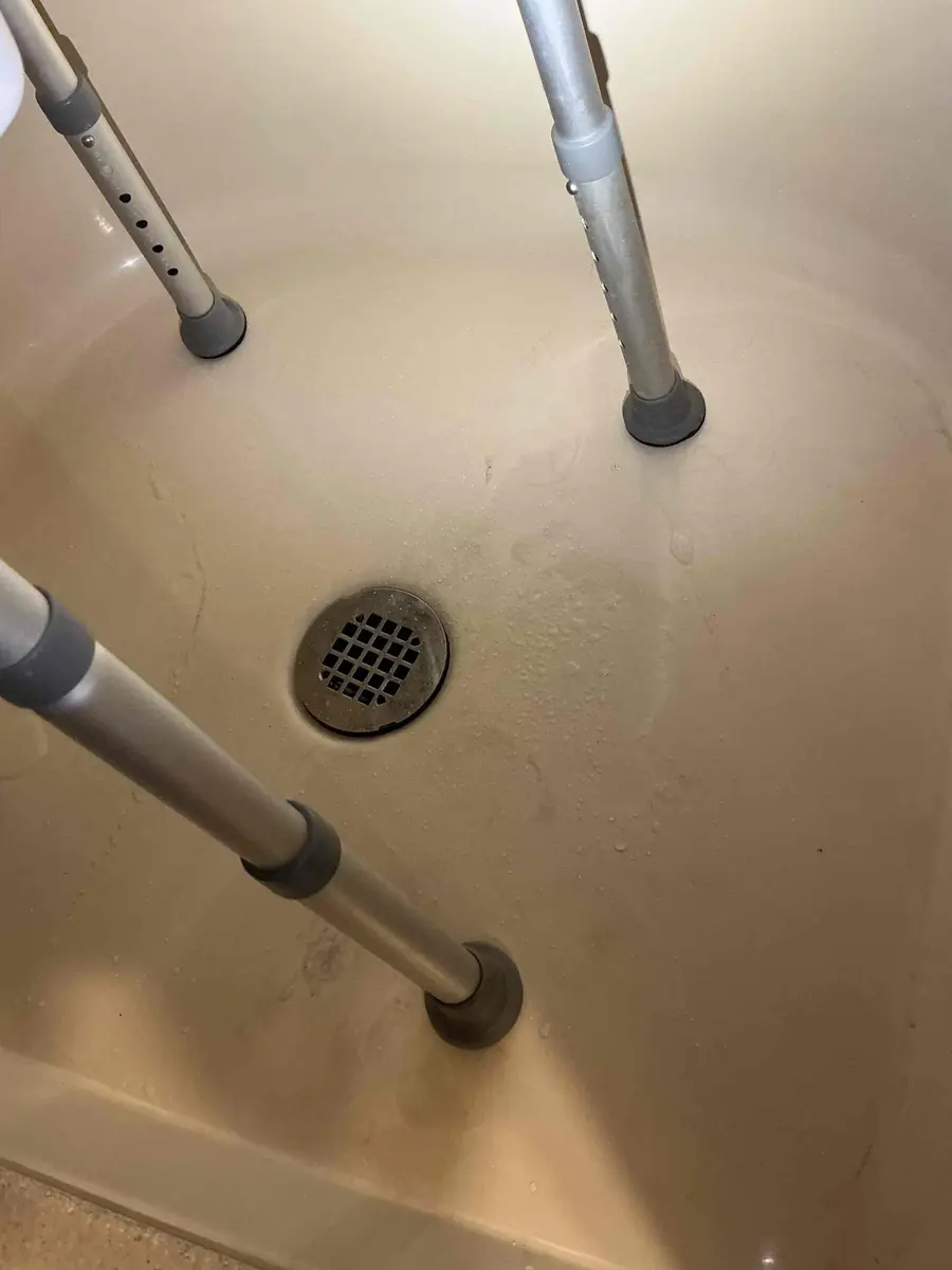 Shower pan with a round chrome screw in drain cover and the legs of a shower chair beside it