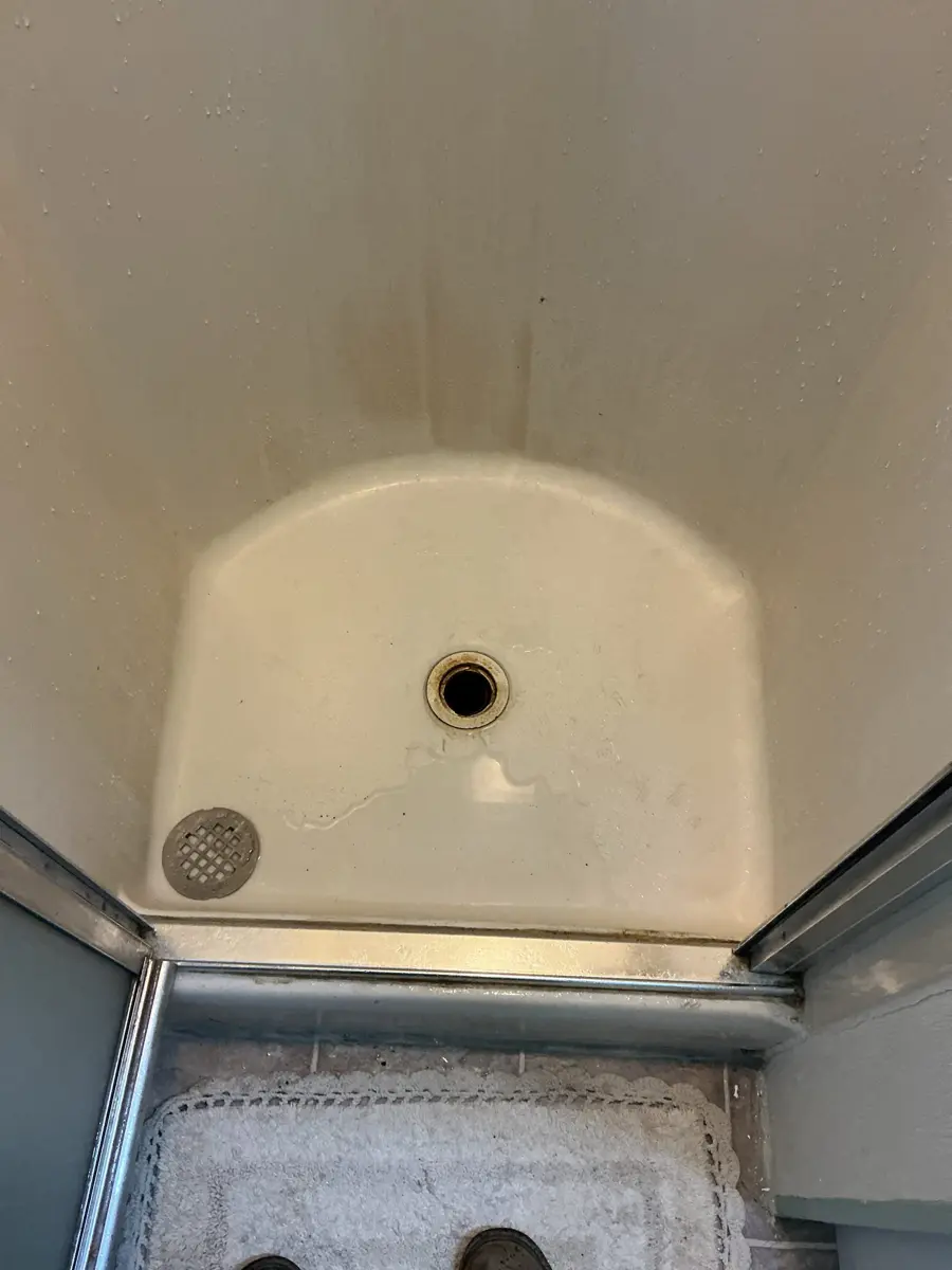 Shower stall pan with the drain cover off and the open drain body visible in the floor