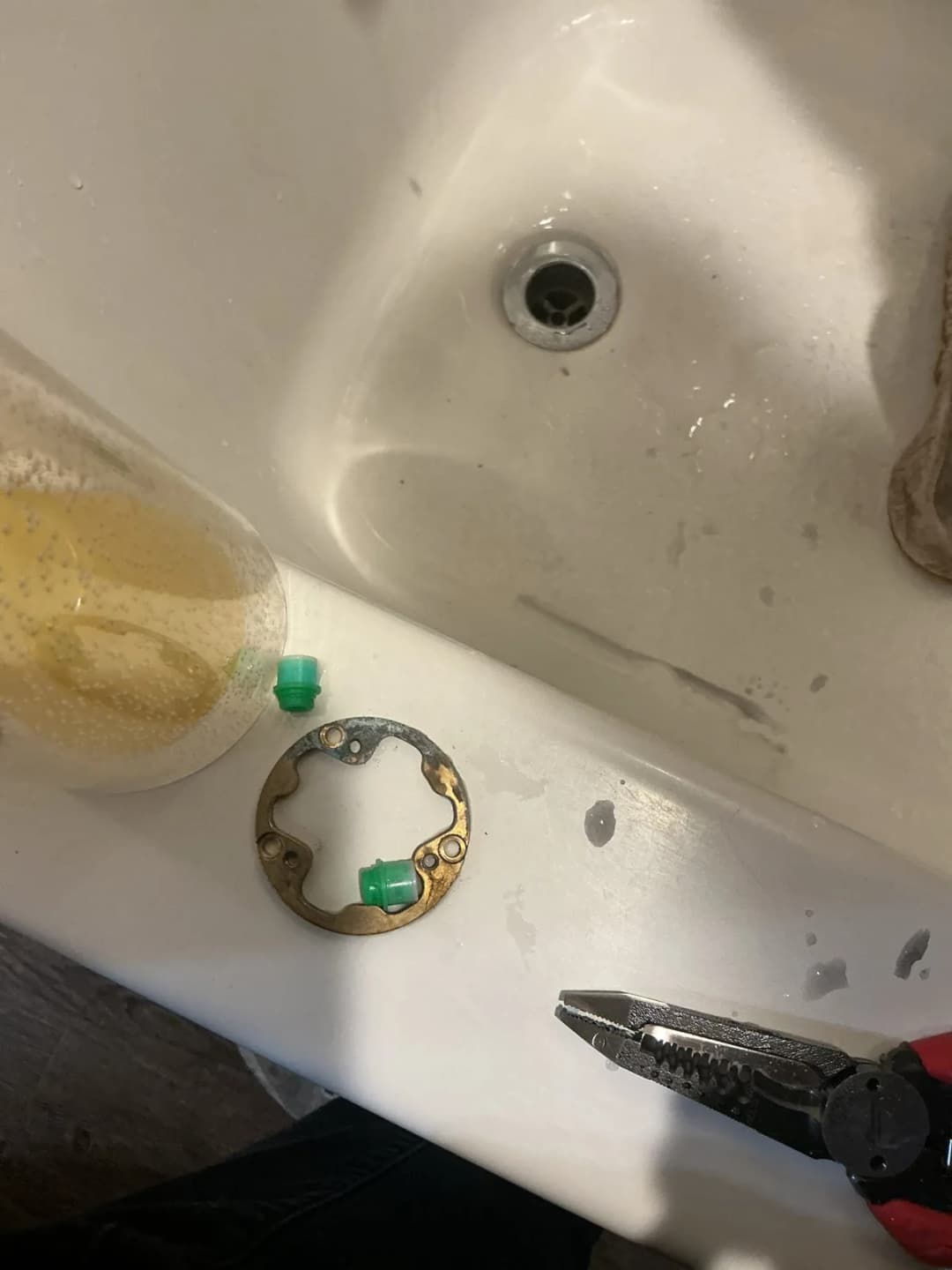 Shower trim parts and retaining ring set on the edge of a bathtub next to pliers