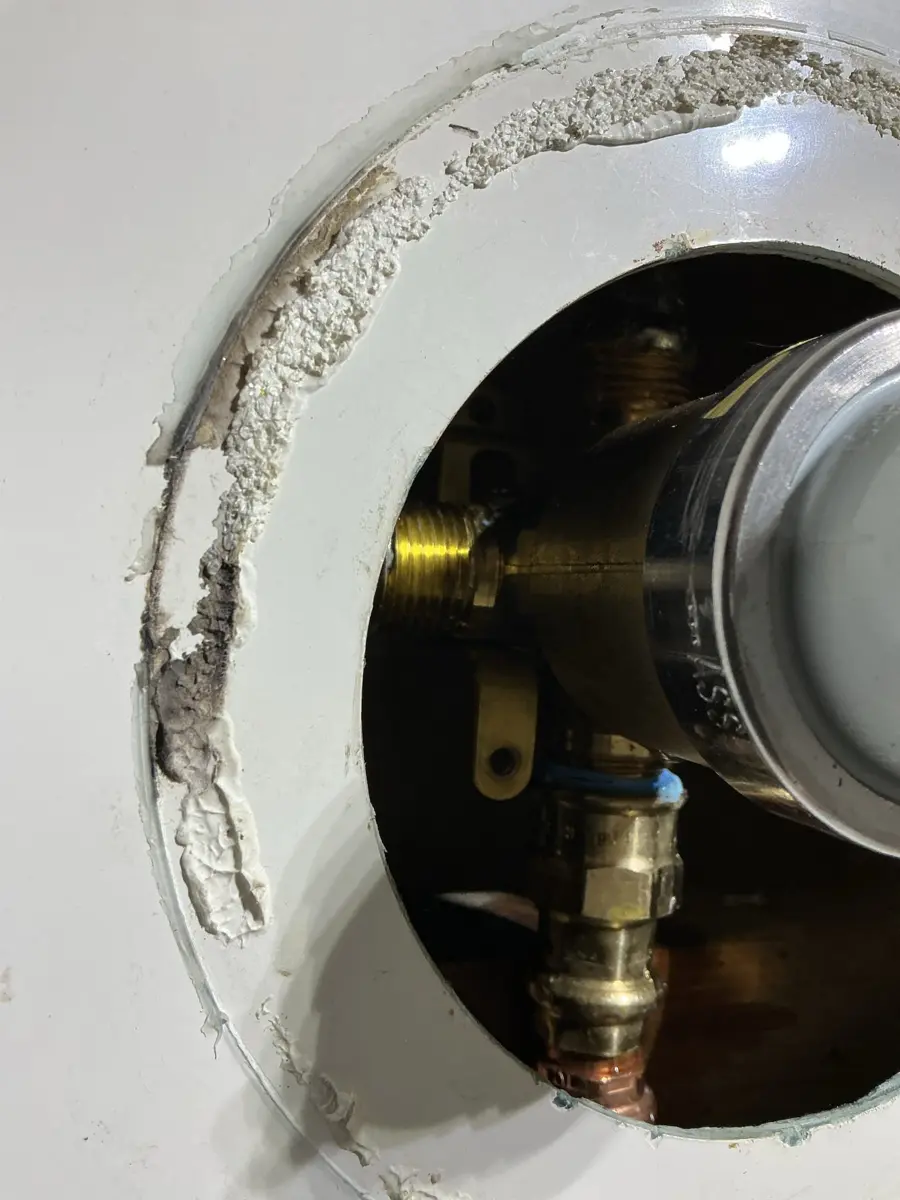 Brass shower valve body seen through the round opening in the shower wall with the trim removed