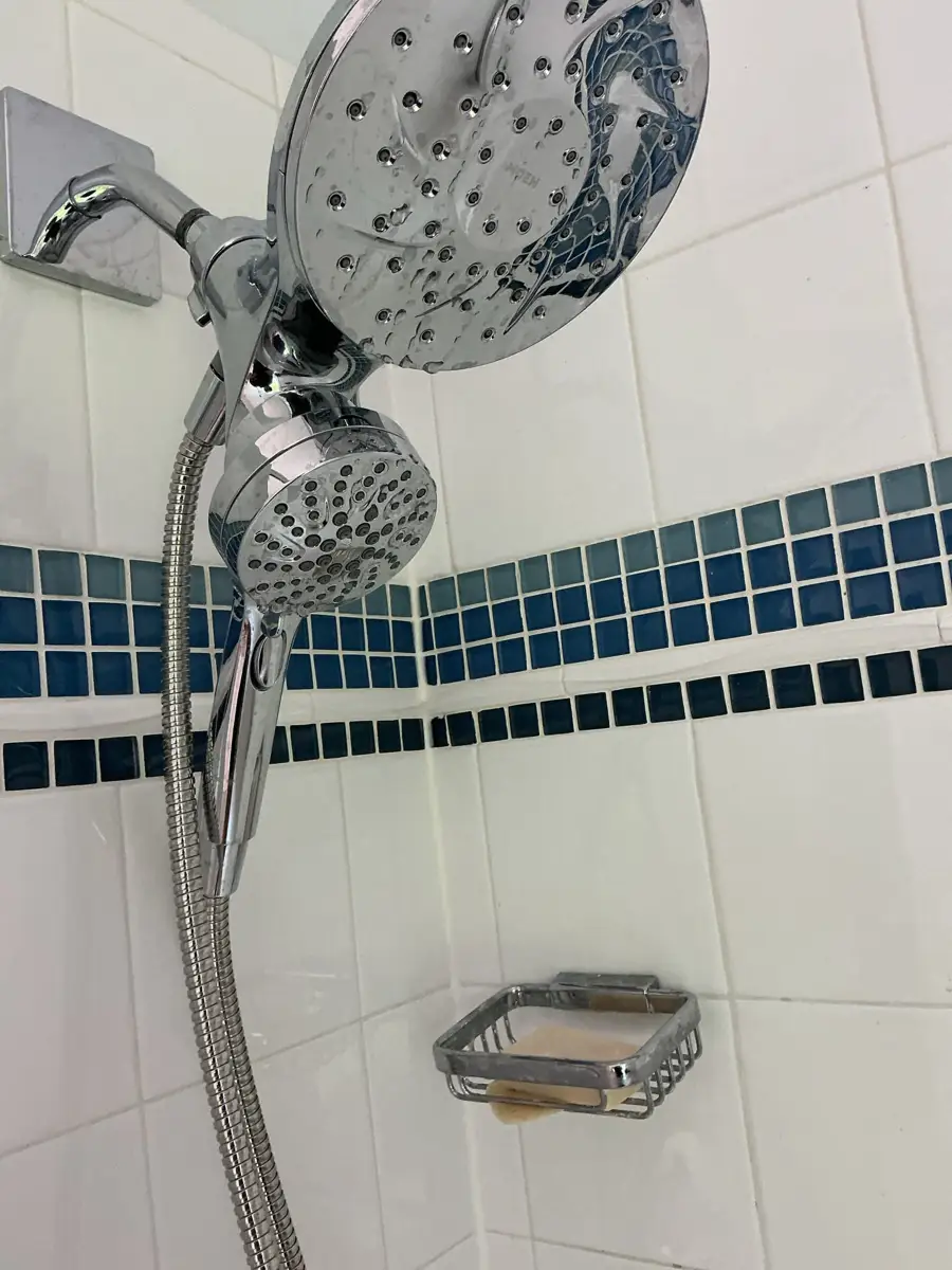 Chrome handheld showerhead on a tiled shower wall where low water pressure was reported