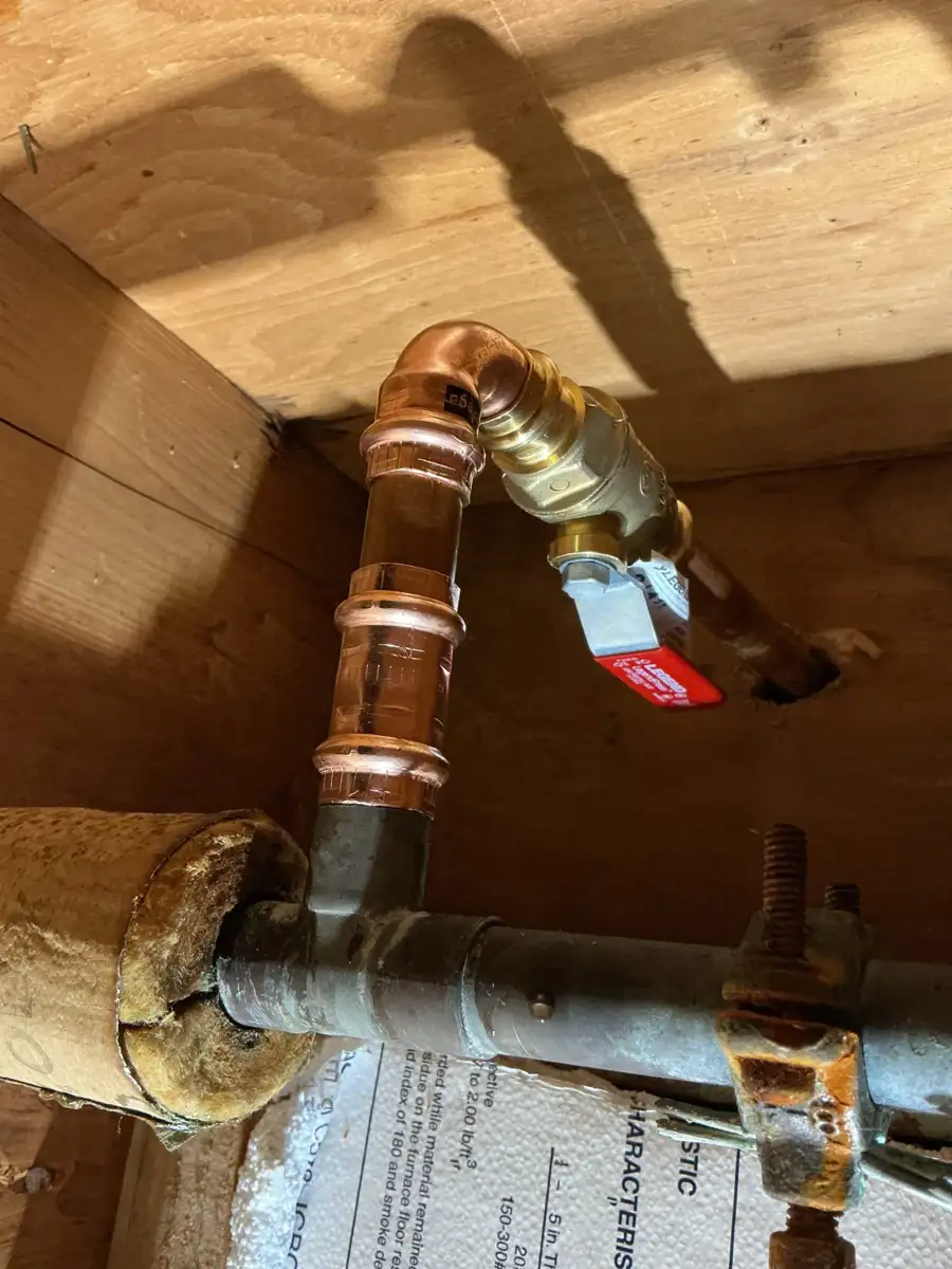 Brass ball valve with a red lever handle on a copper line feeding an outdoor faucet