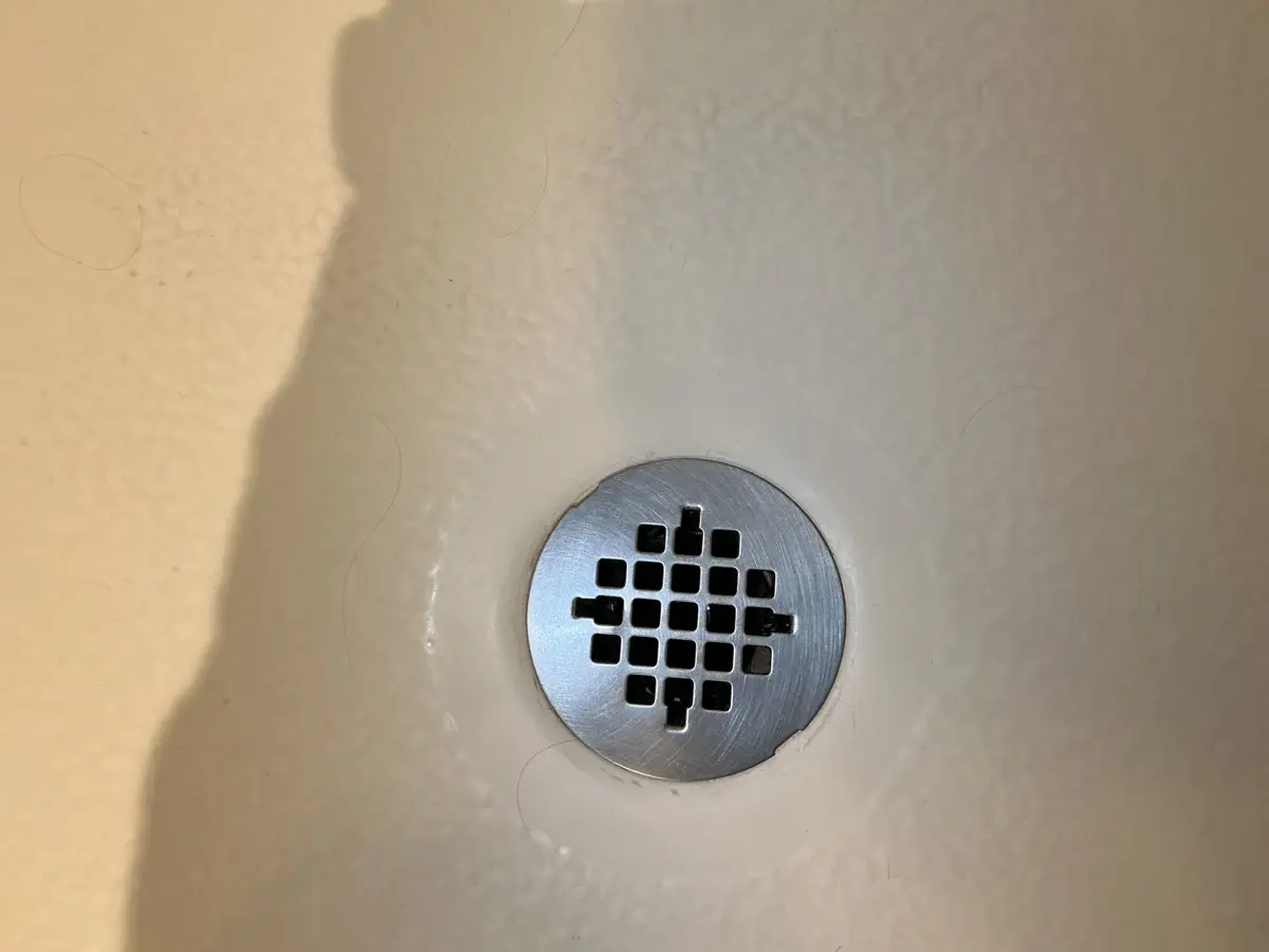 Round stainless snap in shower drain strainer on a white fiberglass shower pan