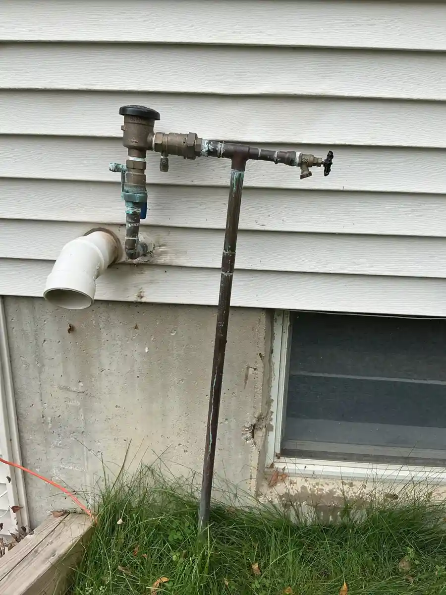 Sprinkler system backflow preventer mounted on an outside wall above the foundation