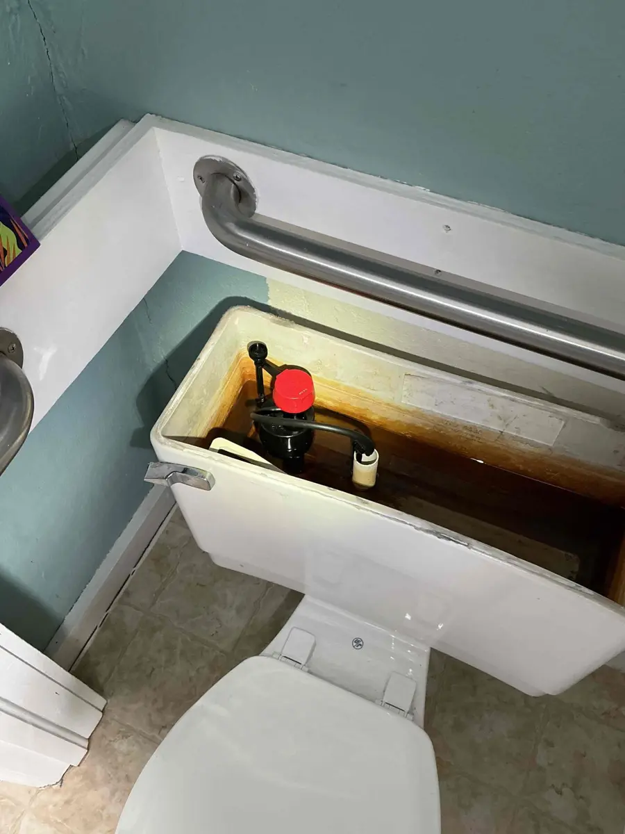 Toilet tank with heavy rust staining at the waterline and a slow filling fill valve