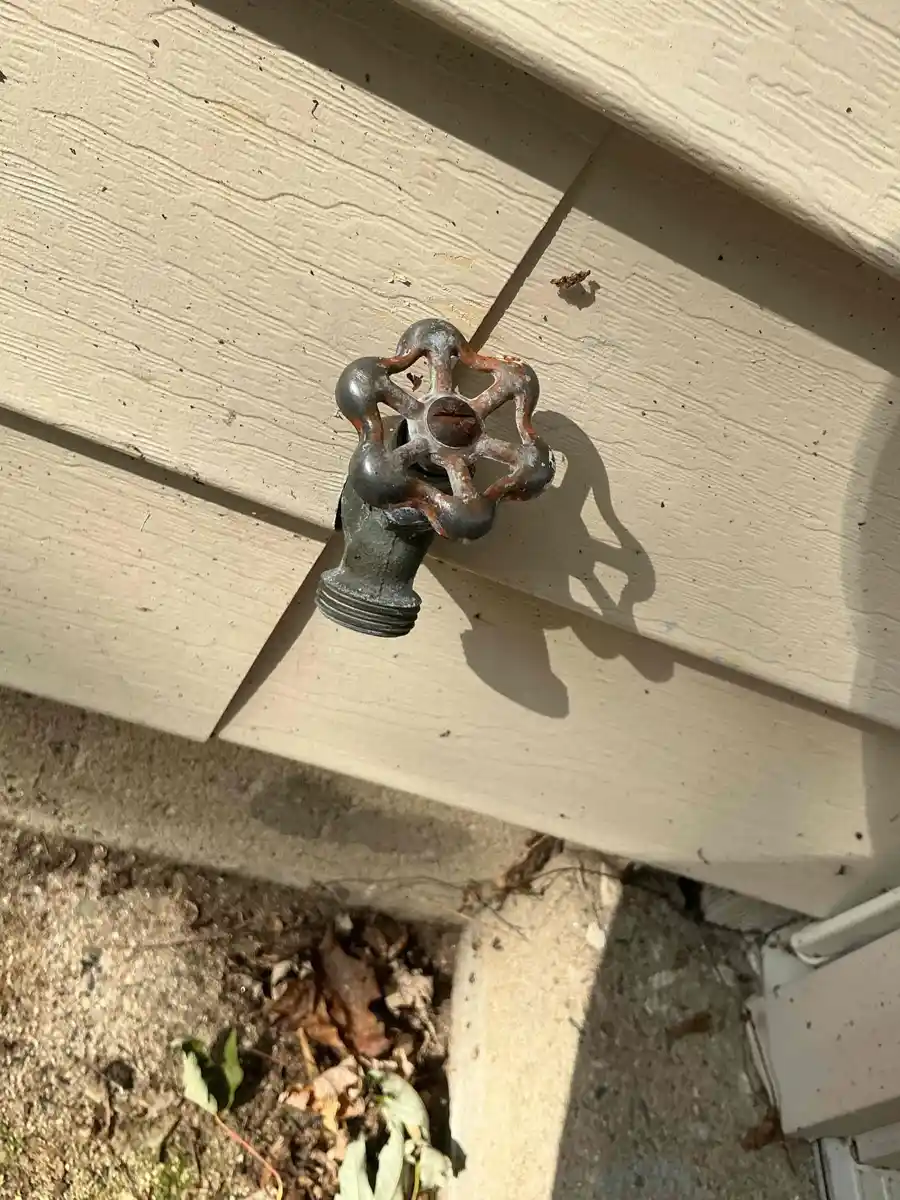Standard outdoor faucet with a round metal handle mounted on house siding