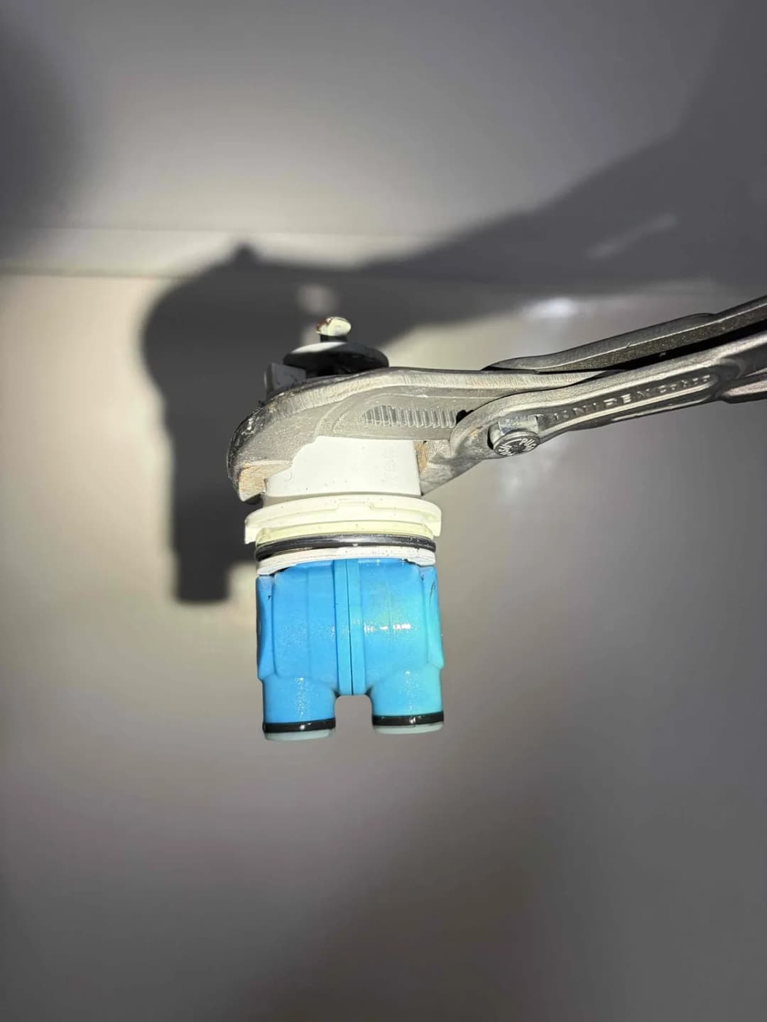 Old shower cartridge gripped with pliers after being pulled from the valve