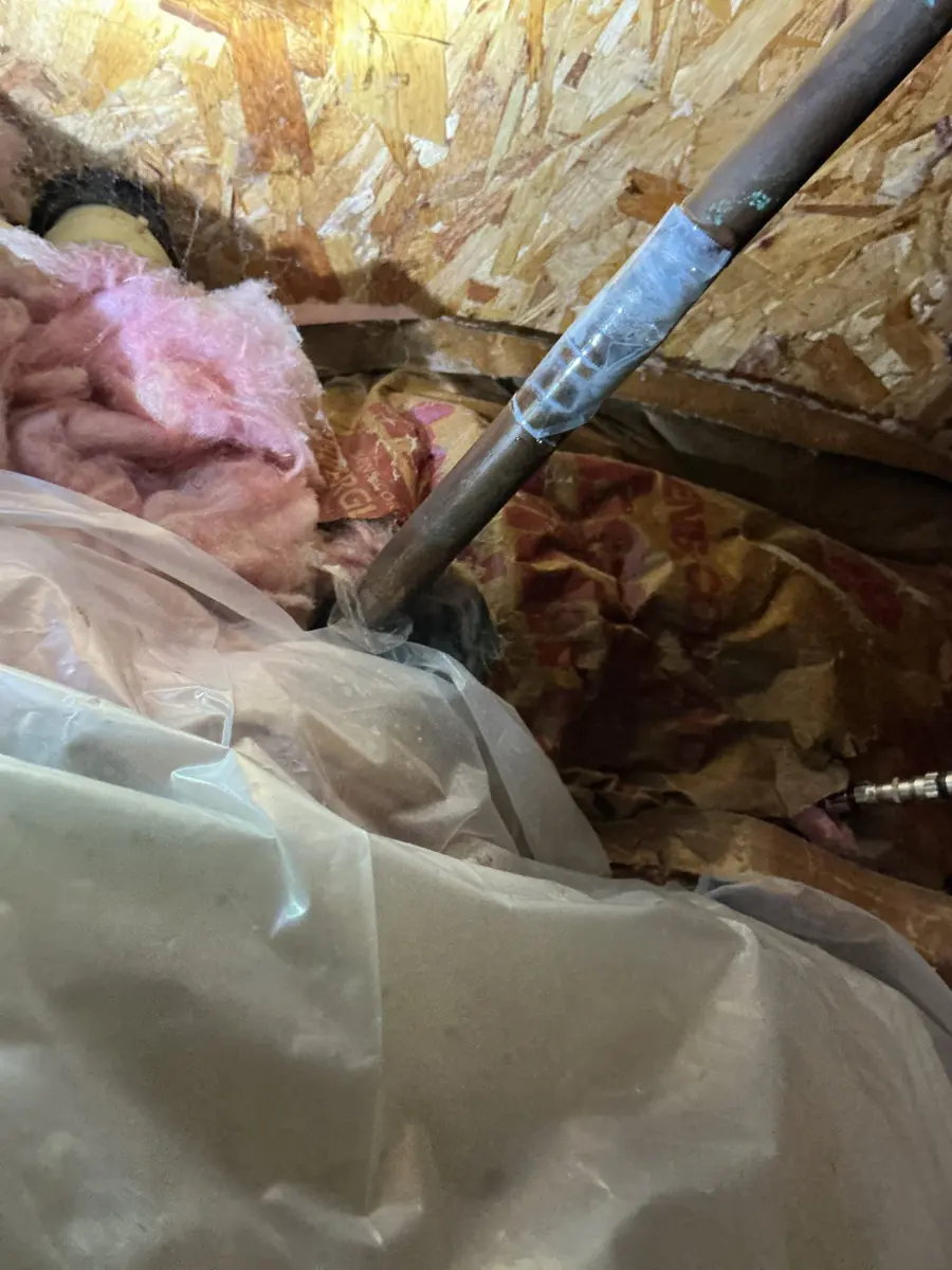 Supply pipe running through pink insulation and plastic sheeting in a basement ceiling near an outside wall