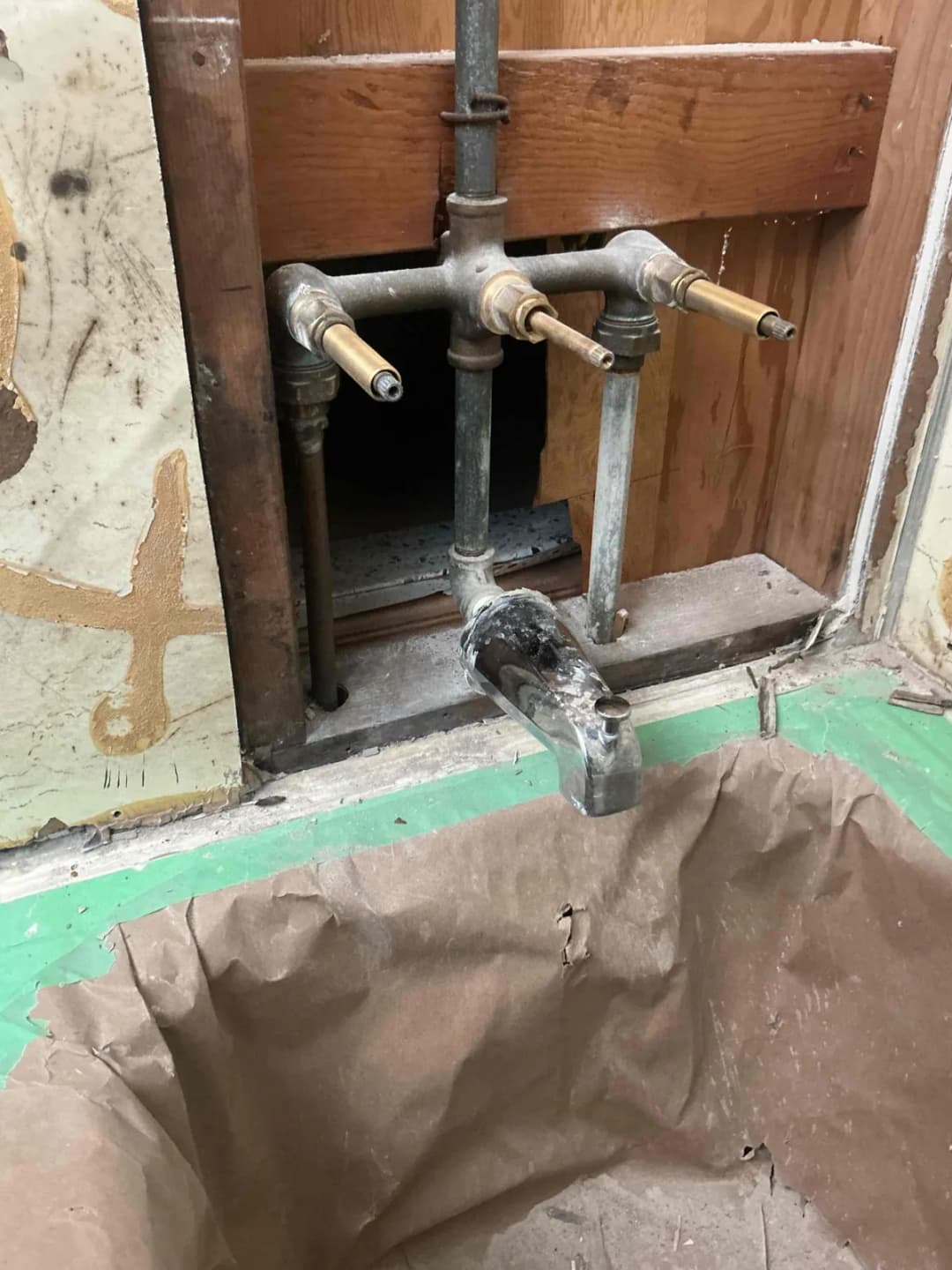 Old three handle shower valve body with copper pipes exposed through an opening in the wall