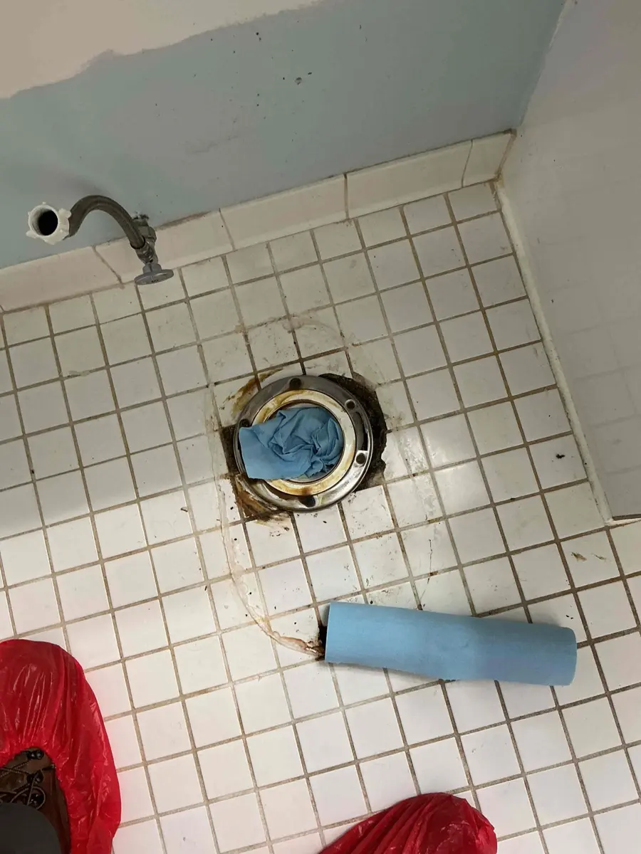 Toilet removed in a tiled bathroom with the floor drain opening plugged with a rag during wax ring repair