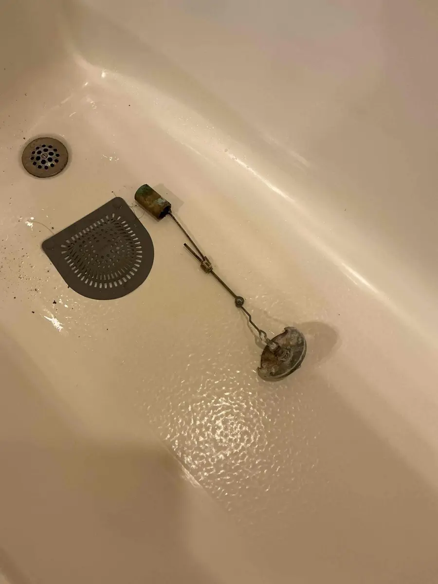 Tub trip lever linkage, drain plug and strainer pulled out and lying in the bathtub