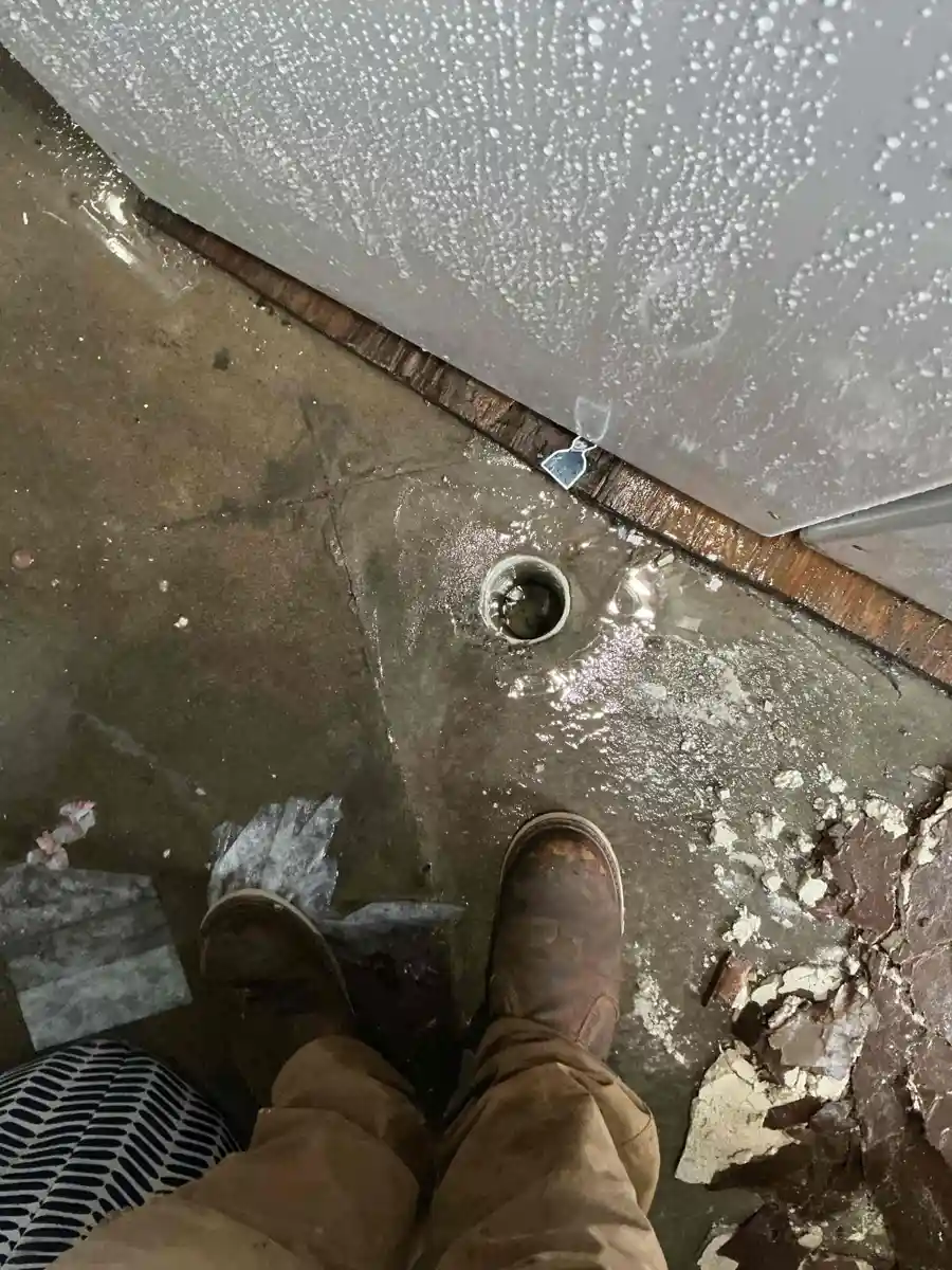 Water spraying down from an opened ceiling onto a wet concrete laundry room floor