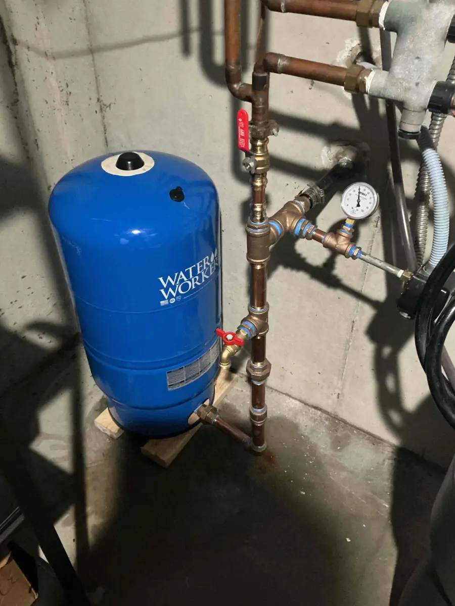 Blue well pressure tank with copper piping and pressure gauge in a basement