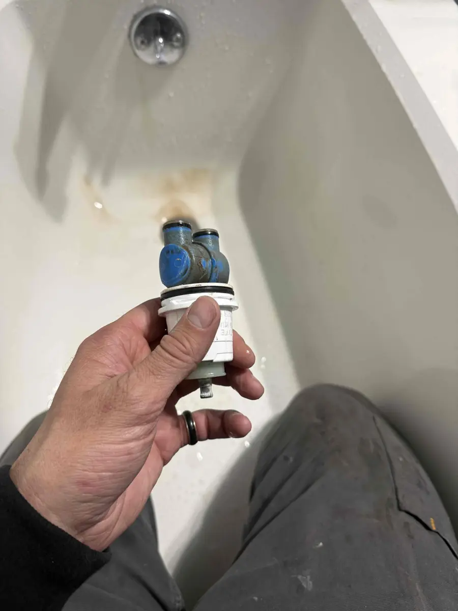 Worn shower cartridge pulled out of the valve and held over the tub
