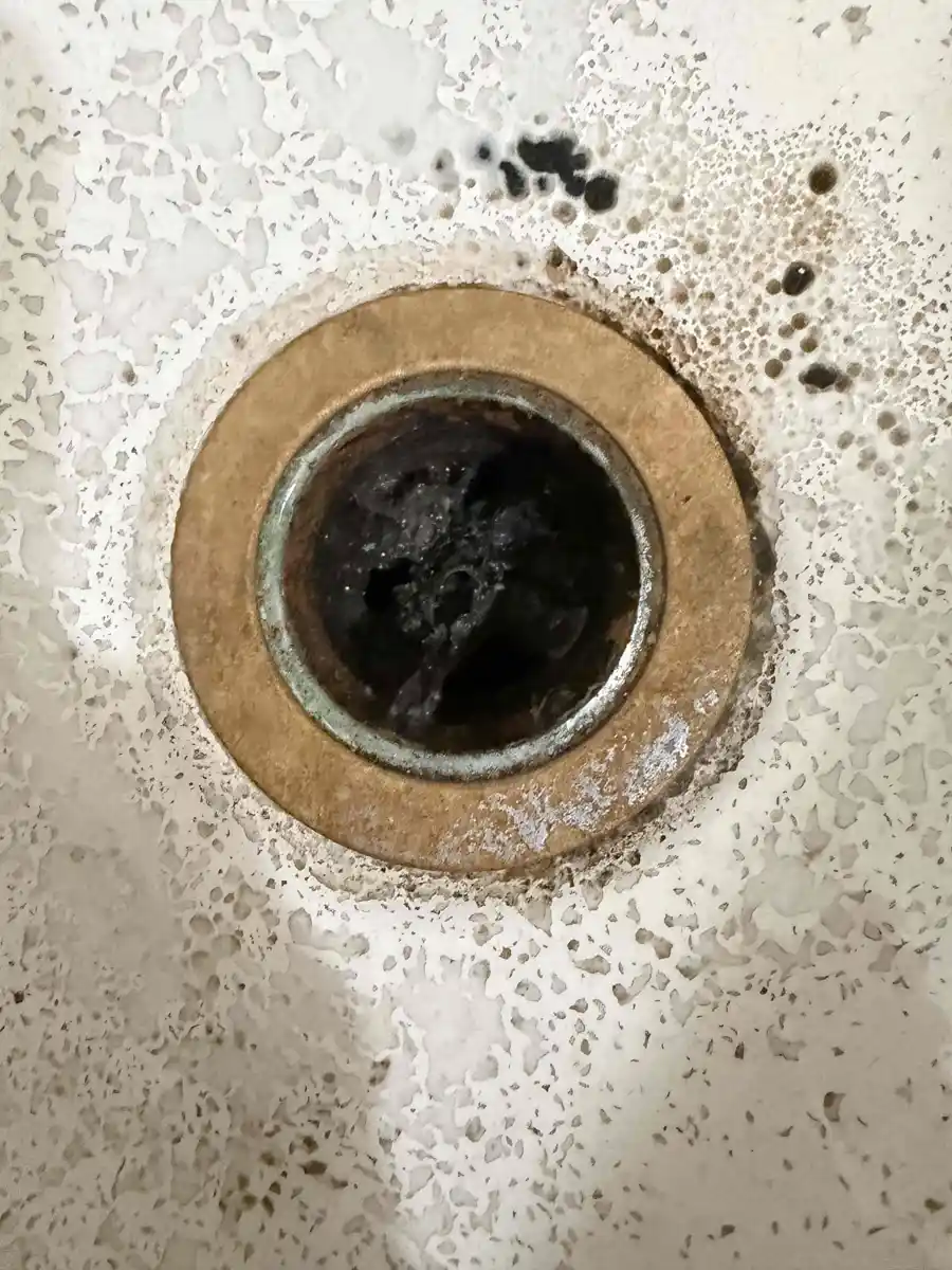 Shower drain opening with the flange removed showing a worn drain body ring and dark buildup inside