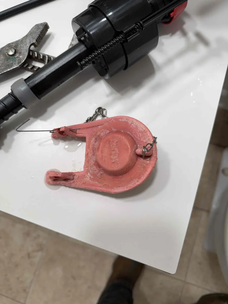 Worn red toilet flapper and old fill valve lying on a counter after being removed from a toilet tank